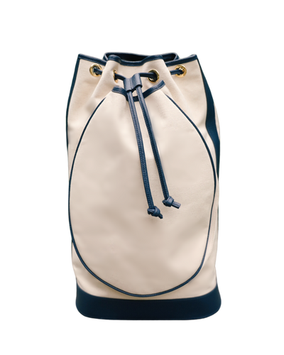 A cream-colored leather bucket bag with dark navy blue trim, drawstring, and base, accented with gold-tone grommets, shown against a plain white background.