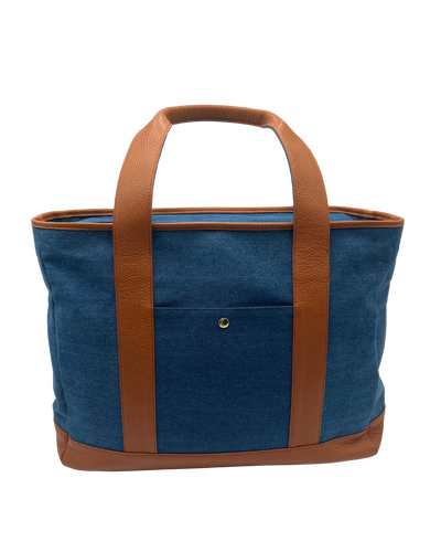 A blue denim tote bag with brown leather handles, trim, and base, shown against a plain white background.