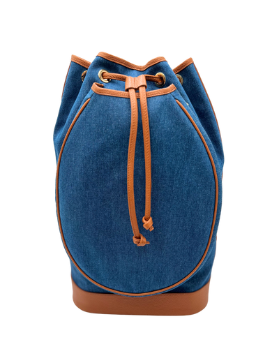 A blue denim bucket bag with tan leather trim, drawstring closure, and a tan leather base, shown against a plain white background.