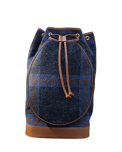 A blue and brown plaid wool bucket bag with tan leather trim, drawstring closure, and a textured leather base, shown against a plain white background.